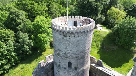Medieval-Bedzin-castle-with-a-turret,-walls,-and-courtyard-during-a-beautiful-summer-day-surrounded-by-lush-greenery,-grass,-and-trees-under-a-clear-blue-sky