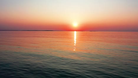 Vista-Derecha-De-Drones-Voladores-Del-Hermoso-Amanecer-Del-Océano-Con-Un-Sol-Brillante-Que-Proyecta-Coloridos-Reflejos-Rojos,-Naranjas,-Morados-Y-Amarillos-Sobre-Las-Ondulantes-Olas-Pacíficas-Del-Mar-Con-Un-Hermoso-Cielo-Y-Agua.