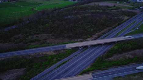 Eine-Ruhige-Dämmerungsszene-Fängt-Lastwagen-Und-Autos-Ein,-Die-über-Die-Autobahn-Fahren,-Umgeben-Von-üppigen-Grünen-Feldern-In-Pennsylvania