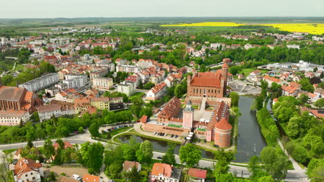 An-expansive-aerial-view-of-Lidzbark-Warmiński,-showcasing-the-town’s-blend-of-historical-and-modern-architecture,-green-areas,-and-a-significant-historical-building-near-a-water-body