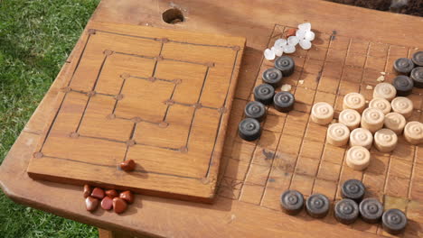 Traditional-strategy-game-setup-with-wooden-pieces-and-carved-board-games,-with-chequers-accompanied-by-a-clay-cup-from-viking-times