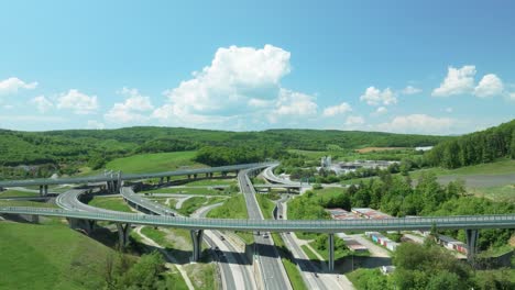 An-aerial-drone-moves-forward-above-an-intricate-tangle-of-a-highway-junction,-showcasing-cars-navigating-complex-roundabouts-and-intersecting-roads