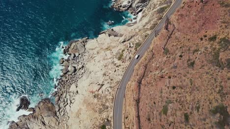 Drone-Siguiendo-Una-Camioneta-Que-Conduce-Por-Una-Pintoresca-Ruta-Costera-En-Ciudad-Del-Cabo,-Sudáfrica