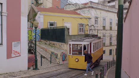Vista-Trasera-De-Viejos-Tranvías-Amarillos-Pasando-Por-El-Elevador-Da-Glória-Durante-El-Día-En-Lisboa,-Portugal