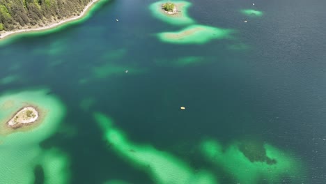 Aerial-of-Eibsee's-vibrant-turquoise-waters-and-small-forested-islands-surrounded-by-lush-green-shores-in-Grainau,-Germany