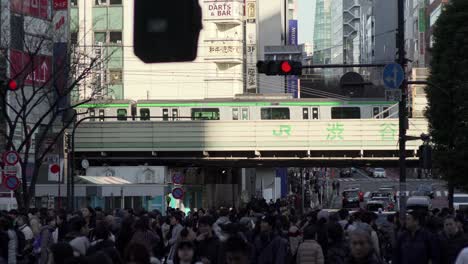 Menschenmassen-Auf-Der-Shibuya-Kreuzung,-Im-Hintergrund-Fährt-Ein-Zug-Der-Yamanote-Linie-Vorbei