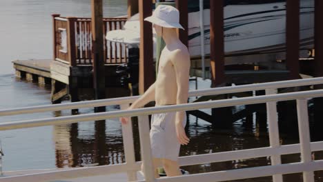 Tracking-shot-of-caucasian-man-walking-to-bathing-jetty,-sitting-and-enjoying-sunlight-in-the-morning