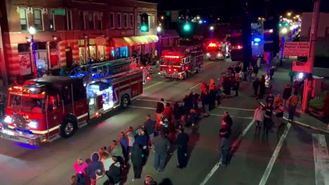 Firetrucks-and-a-police-car-drive-down-the-town's-main-street-in-a-Christmas-parade-at-night