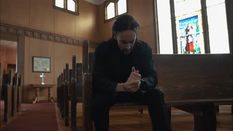 Young,-anxious-man-in-black-suit-sitting-in-pew-in-church-praying-in-worship-in-cinematic-slow-motion