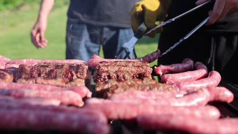 Hand-With-Tongs-Flipping-Sausages-Grilling-Outdoor