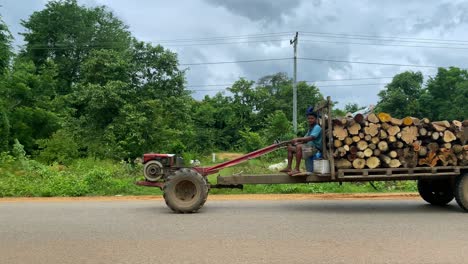 Panoramic-view-of-a-rudimentary-log-transport-on-a-rural-Cambodian-road-on-a-sunny-day-with-clouds-in-the-background