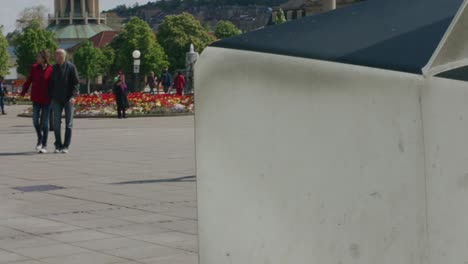 Behind-statue-view-of-couple-holding-hands-as-tourists-pass-by-in-downtown-Stuttgart-Square-at-noon,-Germany,-Europe,-panning-view-angle