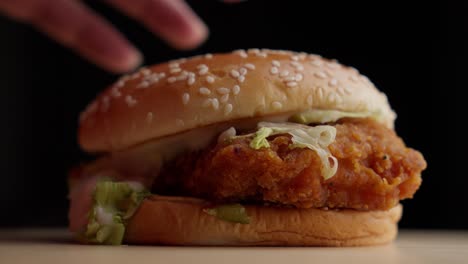 Close-up-studio-shot-Fried-Chicken-Burger,-hands-topping-with-sesame-seeds-bread