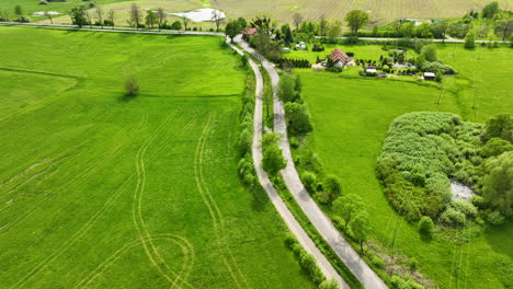 Luftaufnahme-Einer-Kurvenreichen-Landstraße-Durch-Grüne-Felder-Und-Kleine-Siedlungen,-Mit-Ackerland-Im-Hintergrund