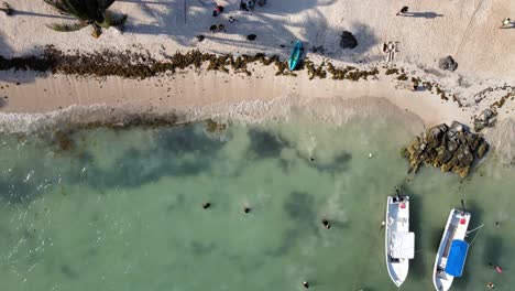 Die-Strandufer-Mit-Touristen,-Schwimmenden-Booten-Und-Dem-Kristallklaren-Wasser,-Das-Den-Weißen-Sand-Erreicht
