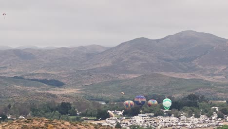 Temecula-Balloon-and-Wine-Festival-Grounds-Four-Tethered-Hot-Air-Balloons-Shot-by-Drone-with-no-movement-Paragliders-sailing-around