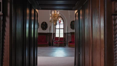 Peek-through-ornate-wooden-doors-into-Chivalric-Hall-of-Trakoscan-Castle,-showcasing-regal-red-themed-interior