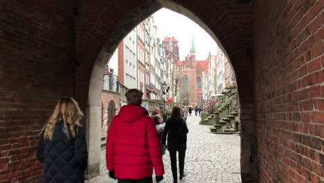 Mirando-Hacia-La-Basílica-De-San-Mayo-Desde-El-Arco-Medieval-A-Lo-Largo-De-Una-Calle-Adoquinada-Llamada-Mariacka,-Gdansk,-Polonia,-En-Un-Frío-Día-De-Invierno-Con-Turistas-Caminando