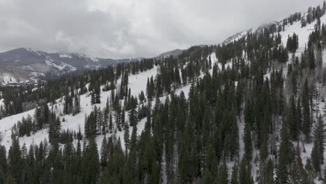 Aerial-pan-up-of-snowy-mountains-and-forest-near-Solitude-Resort-in-Big-Cottonwood-Canyon,-Utah-during-late-spring