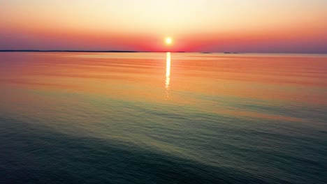 Beautiful-Ocean-Sunrise-with-Bright-Glowing-Sun-Casting-Colorful-Red,-Orange,-Purple-and-Yellow-Reflections-Over-Peaceful-Rippling-Waves-of-the-Sea