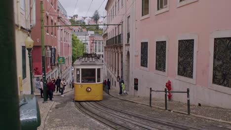 Front-view-of-yellow-old-tram-driving-up-the-slope-in-Lisbon,-Portugal