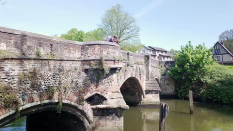 Woman-stood-on-medieval-arched-Bishops-bridge-looking-over-parapet-into-river-Wensum