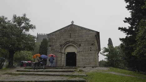 Tourists-hold-up-umbrellas-as-they-walk-on-guided-tour-on-rainy-day-past-stone-chapel