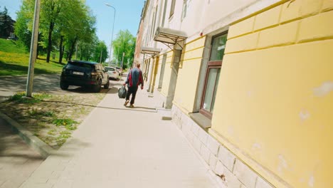 Borracho-Caminando-Por-Una-Calle-Luminosa-Y-Soleada-Llevando-Una-Bolsa-De-Plástico-Vista-Trasera-Pov-De-ángulo-Holandés