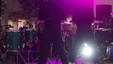 Two-young-man-hitting-drum-plates-and-cymbals-on-a-music-stage-against-white-spotlight