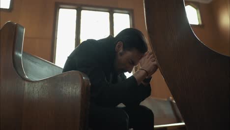 Young-man-in-black-suit-praying-in-church-in-cinematic-slow-motion