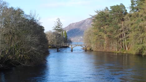 Vista-Panorámica-Del-Idílico-Puente-De-Madera-Sobre-El-Río-Oich-Hacia-El-Lago-Ness-Desde-Fort-Augustus-En-Las-Tierras-Altas-De-Escocia,-Reino-Unido