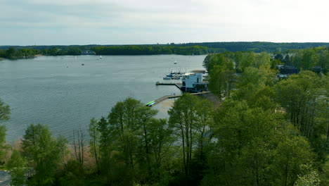 An-aerial-view-of-Ukiel-Lake-in-Olsztyn,-highlighting-the-marina-area-with-boats-and-green-trees,-showing-a-panoramic-view-of-the-lake