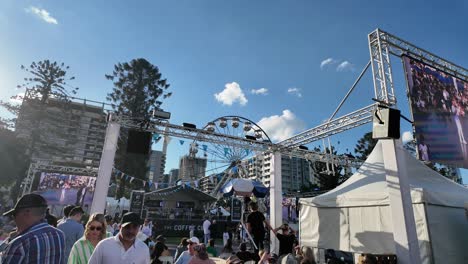 Menschen-Entspannen-Beim-Griechischen-Paniyiri-Festival-Mit-Bühne-Und-Riesenrad-Im-Hintergrund