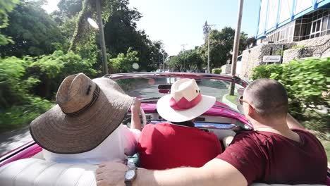 group-of-friends-local-and-tourist-drive-fast-around-the-street-of-havana-driving-a-old-fashioned-red-cabrio-car