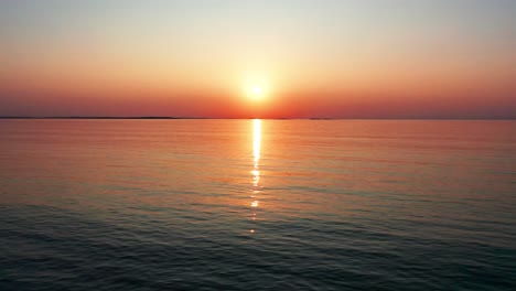 Aerial-Drone-View-of-Gorgeous-Ocean-Sunrise-with-Bright-Glowing-Sun-Casting-Colorful-Red,-Orange,-Purple-and-Yellow-Reflections-Over-Peaceful-Rippling-Waves-of-the-Sea-with-Beautiful-Sky-and-Water