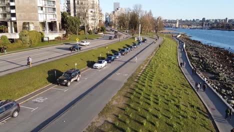 Luftaufnahme-über-Dem-Uferdamm-Am-Sonnenuntergangsstrand-Des-Beliebten-Parks-In-Der-Innenstadt-Von-Vancouver,-Während-Menschen-In-Gruppen-Vorbeigehen,-Ohne-Auf-Die-Nähe-Zu-Achten,-Keine-Masken-Zu-Tragen-Und-Die-Regeln-Zur-Sozialen-Körperlichen-Distanzierung-Zu-Ignorieren