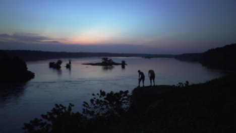 Männer-Mit-Stirnlampe-In-Der-Abenddämmerung,-Gehen-Und-Sitzen-Am-Ufer-Des-Nils-In-Der-Nähe-Von-Jinja,-Uganda