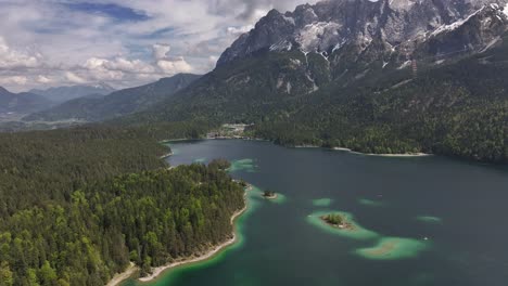 Aerial-view-of-Eibsee-lake-surrounded-by-lush-green-forests-and-majestic-snow-capped-mountains-under-a-partly-cloudy-sky-in-Grainau,-Germany