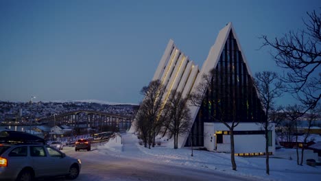 Cars-driving-on-snowy-road-beside-modern-arctic-cathedral-in-Tromso,Norway-during-Christmas-Time