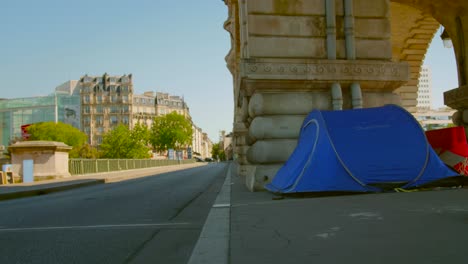 Un-Pequeño-Campamento-De-Refugiados-Sin-Hogar-Que-Duermen-En-Tiendas-De-Campaña-Bajo-Un-Ferrocarril-En-El-Puente-Bir-Hakeim-En-Una-Intersección-En-París,-Francia.