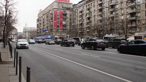 Tráfico-Urbano-En-El-Centro-De-Bucarest-Con-Arquitectura-Moderna-Y-Clásica,-Día-Nublado