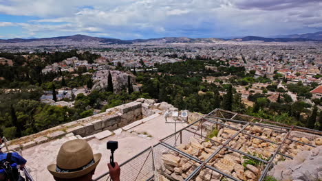 High-angle-shot-of-tourists-coming-down-from-top-of-Monument-of-Agrippa-in-Athens,-Greece,-with-stone-rampart-against-downtown-houses-on-a-cloudy-day
