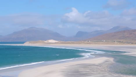 Pan-of-coastal-landscape-at-low-tide-and-blue-ocean-with-mountains-in-the-distance-on-the-remote-isle-of-Lewis-and-Harris-in-Outer-Hebrides,-Western-Scotland-UK