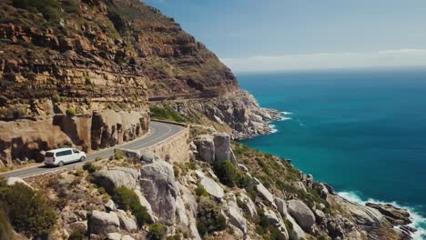 Drone-Volando-Con-Una-Camioneta-Blanca-En-Una-Pintoresca-Ruta-Costera-En-Ciudad-Del-Cabo,-Sudáfrica