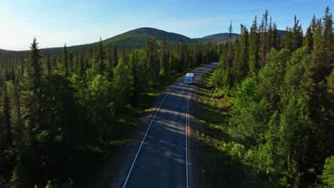 Drone-shot-over-a-Camper-van-on-a-arctic-forest-road,-driving-toward-fells,-summer-evening