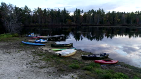 Fast-panning-drone-shot-of-empty-boats-and-canoes-on-the-shore-of-a-beautiful-pond