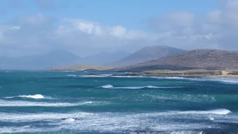 Scenic-seascape-view-of-wild-waves-with-spray-rolling-in-over-blue-ocean-with-mountainous-terrain-on-the-isle-of-Lewis-and-Harris,-Outer-Hebrides,-Western-Scotland-UK