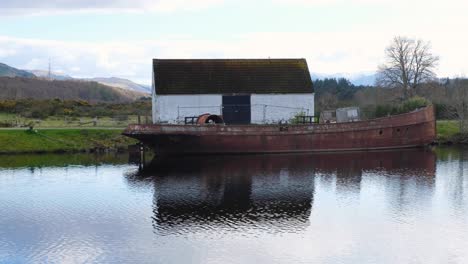 Vista-Panorámica-Del-Canal-De-Caledonia,-Antigua-Barcaza-Abandonada-Y-Cabaña-De-Piedra-Tradicional,-En-Fort-Augustus,-Highlands-De-Escocia,-Reino-Unido