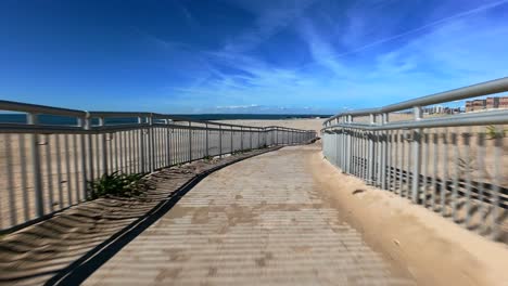 Low-angle-view-of-an-FPV-drone-flying-fast-backwards-over-an-empty-beach-on-a-sunny-day-with-blue-skies