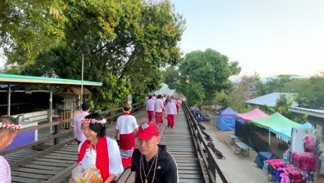 Establishing-in-slow-motion-of-a-group-of-people-walking-in-typical-Thai-clothes-on-a-wooden-bridge,-Sangkhlaburi-Thailand